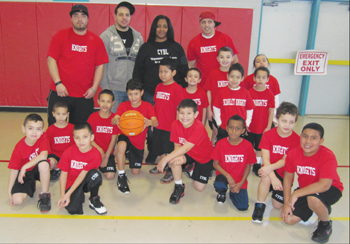 Chelsea Youth Basketball League President Michelle Lopez (back row, second from right) joins Scarlet Knights coaches Dennis McCann, Troy Irizarry, and Tommy Santiago and players for a photo after their game Saturday at the Williams Middle School gymnasium.