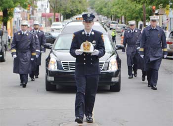 Young Charlie Crowley - a firefighter in New Hampshire - is seen carrying his father's fire helmet ahead of the hearse during a procession up Broadway last Saturday during a memorial to fourth-generation Chelsea Firefighter Charlie Crowley Jr. Crowley - a deputy chief - was only 56 when he died suddenly on June 3rd.